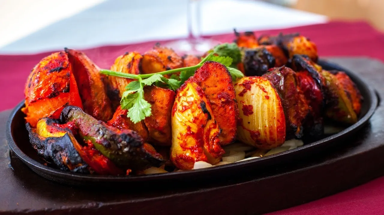 Grilled marinated meat pieces with herbs on a black sizzling platter