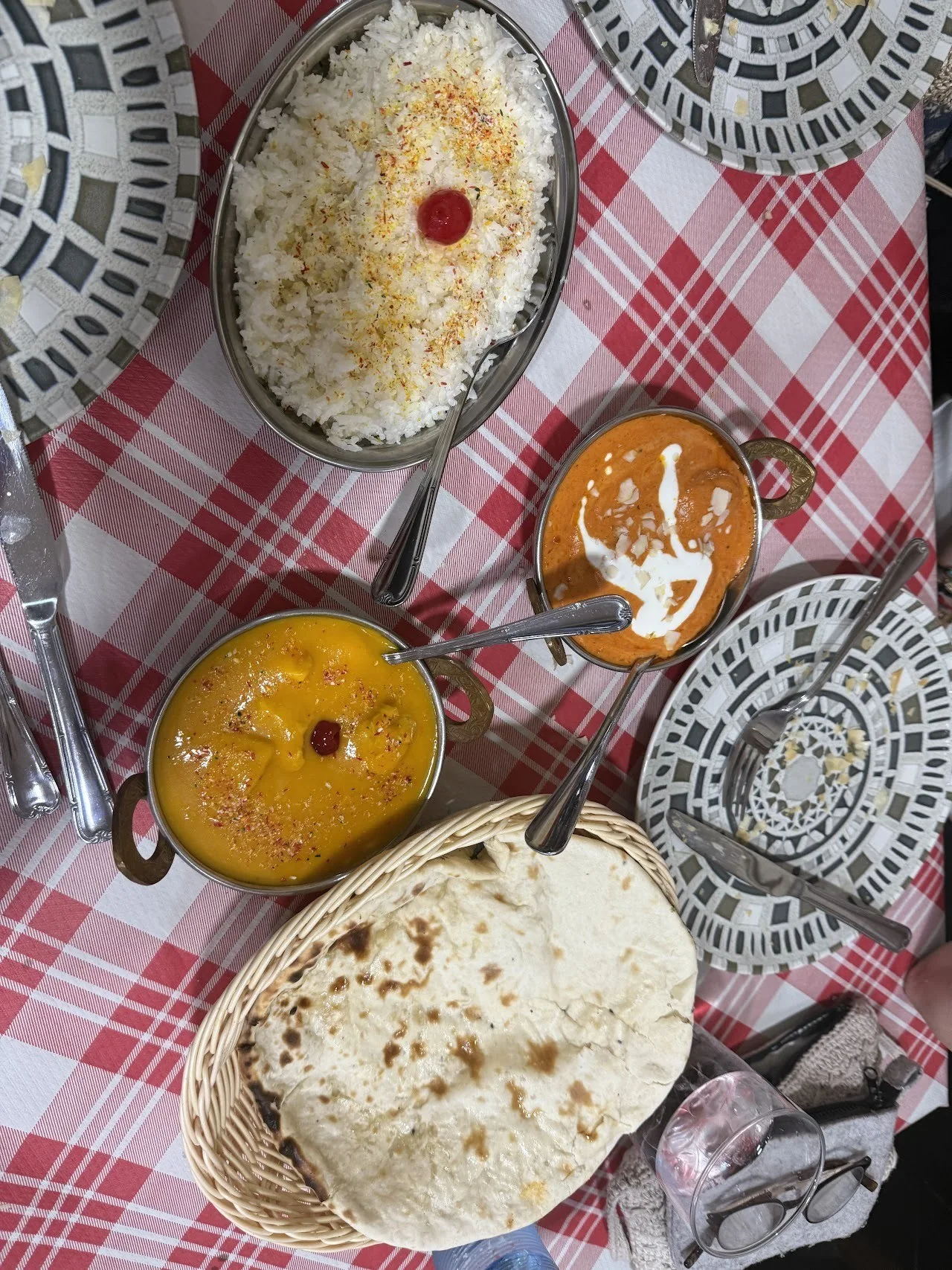 An overhead view of bowls of curry, rice and naan on a red checked tablecloth