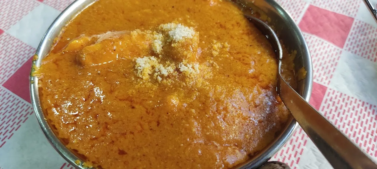 A metal bowl of orange curry sauce garnished with cheese