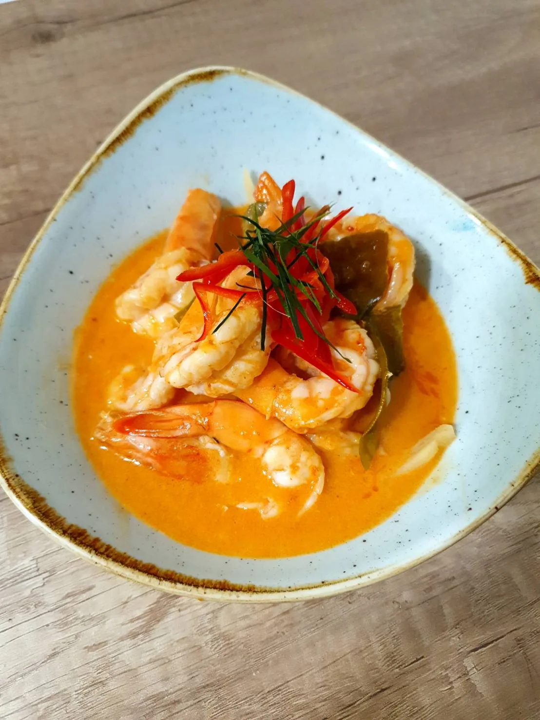 A bowl of shrimp in orange curry sauce with chili