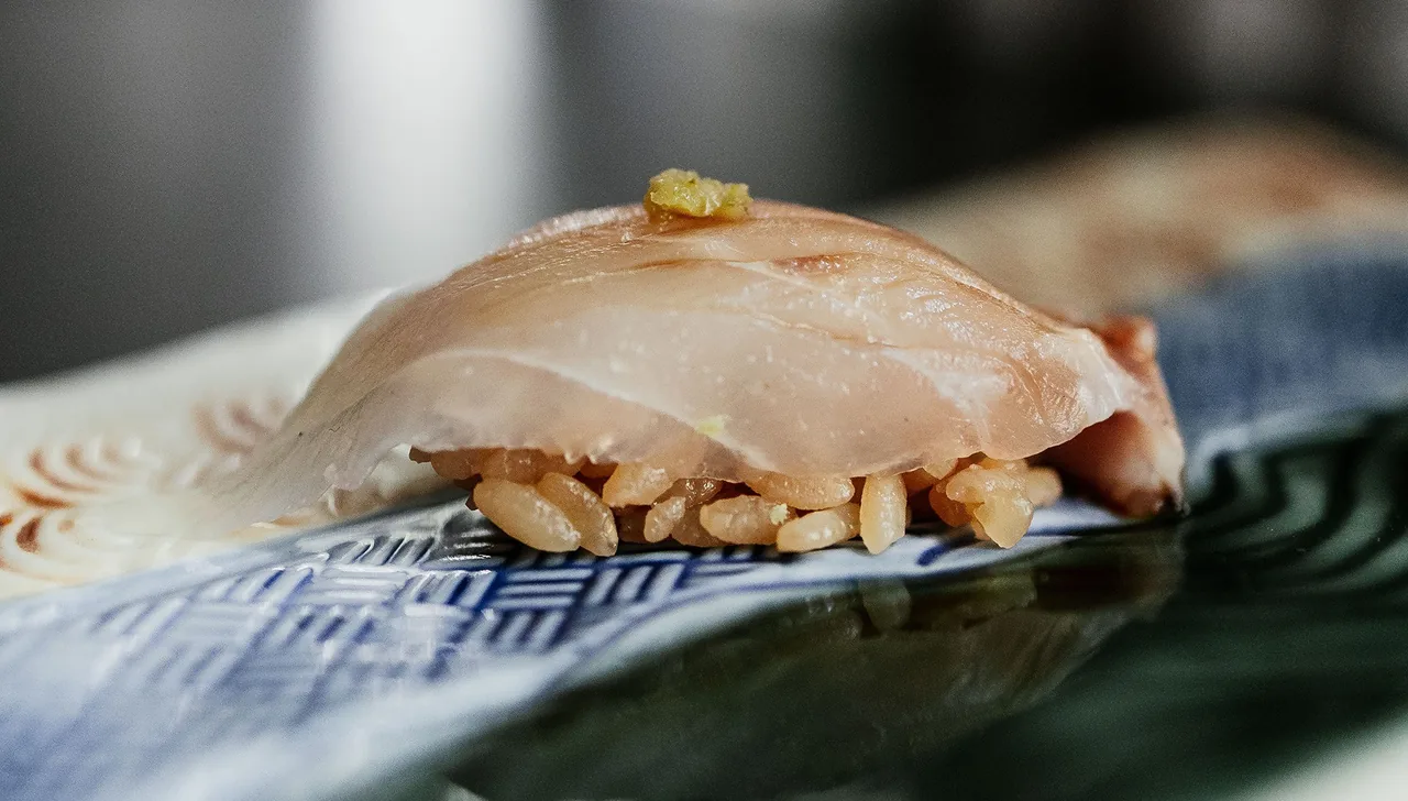 A piece of pale fish nigiri on a blue patterned plate