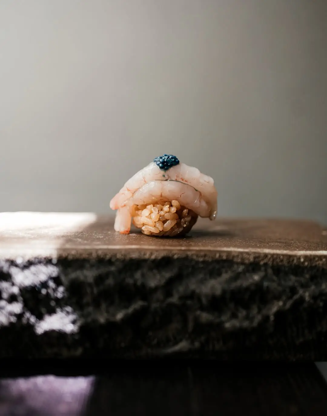 Shrimp nigiri topped with blue caviar against a plain background