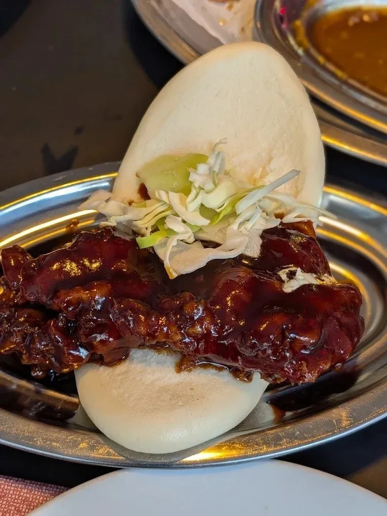 A white steamed bun filled with glazed meat and shredded cabbage