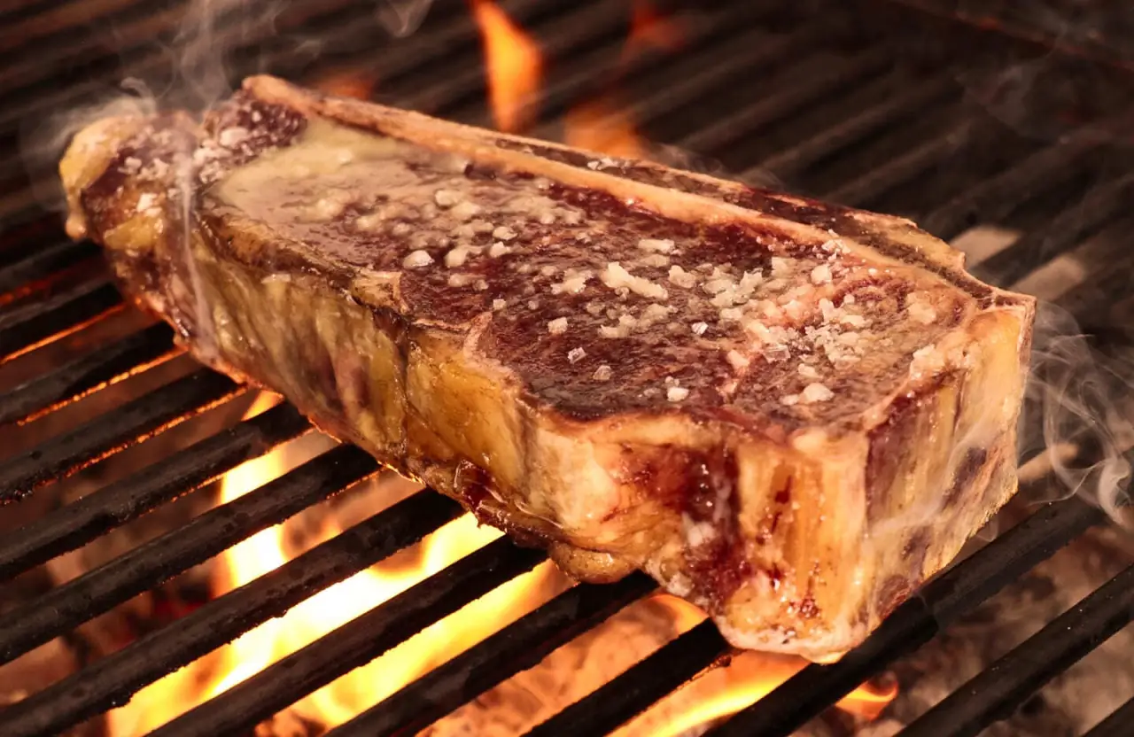 Large bone-in beef steak crusted with coarse salt searing over open flames on a grill grate