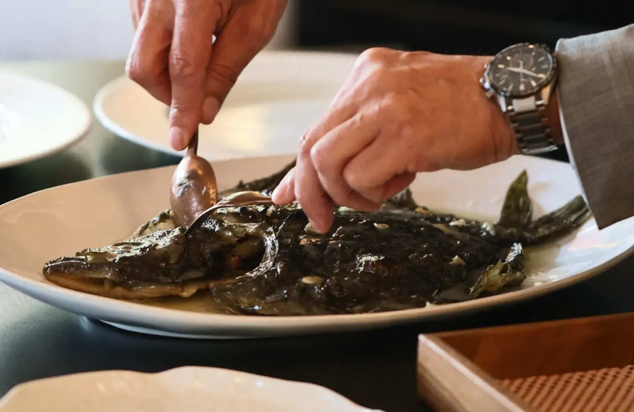 Whole grilled turbot on a white platter being deboned and served tableside with a spoon