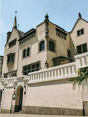 Exterior of a historic gabled stone mansion with a balustraded wall in daylight