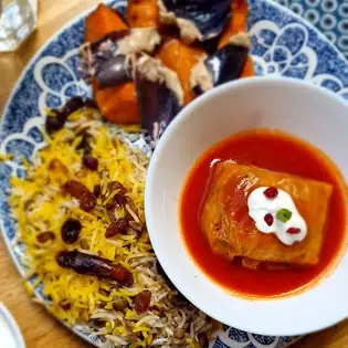 Plate of saffron rice studded with barberries beside roasted aubergine with tahini and a stuffed dish in tomato sauce topped with yogurt on a blue-patterned plate
