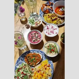 Wooden table laid with an array of Persian small plates and dips, saffron rice, salads and tall glasses of iced herb drinks