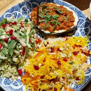 Blue-patterned plate holding a pomegranate-topped bulgur salad, a spiced aubergine dish and saffron rice flecked with barberries and shredded carrot
