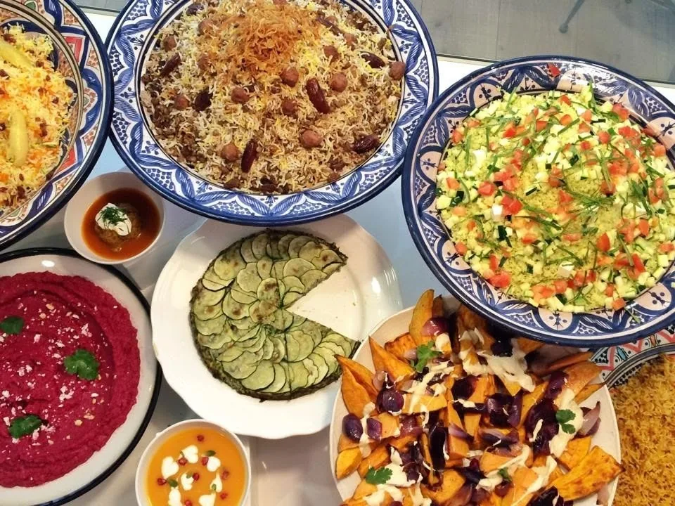 A table with a spread of rice dishes, salads, dips and a dark red beetroot dip in patterned bowls