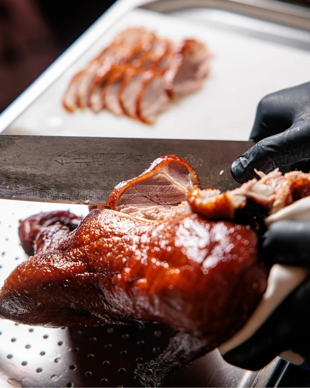 A chef in black gloves carving a roast duck with slices behind it