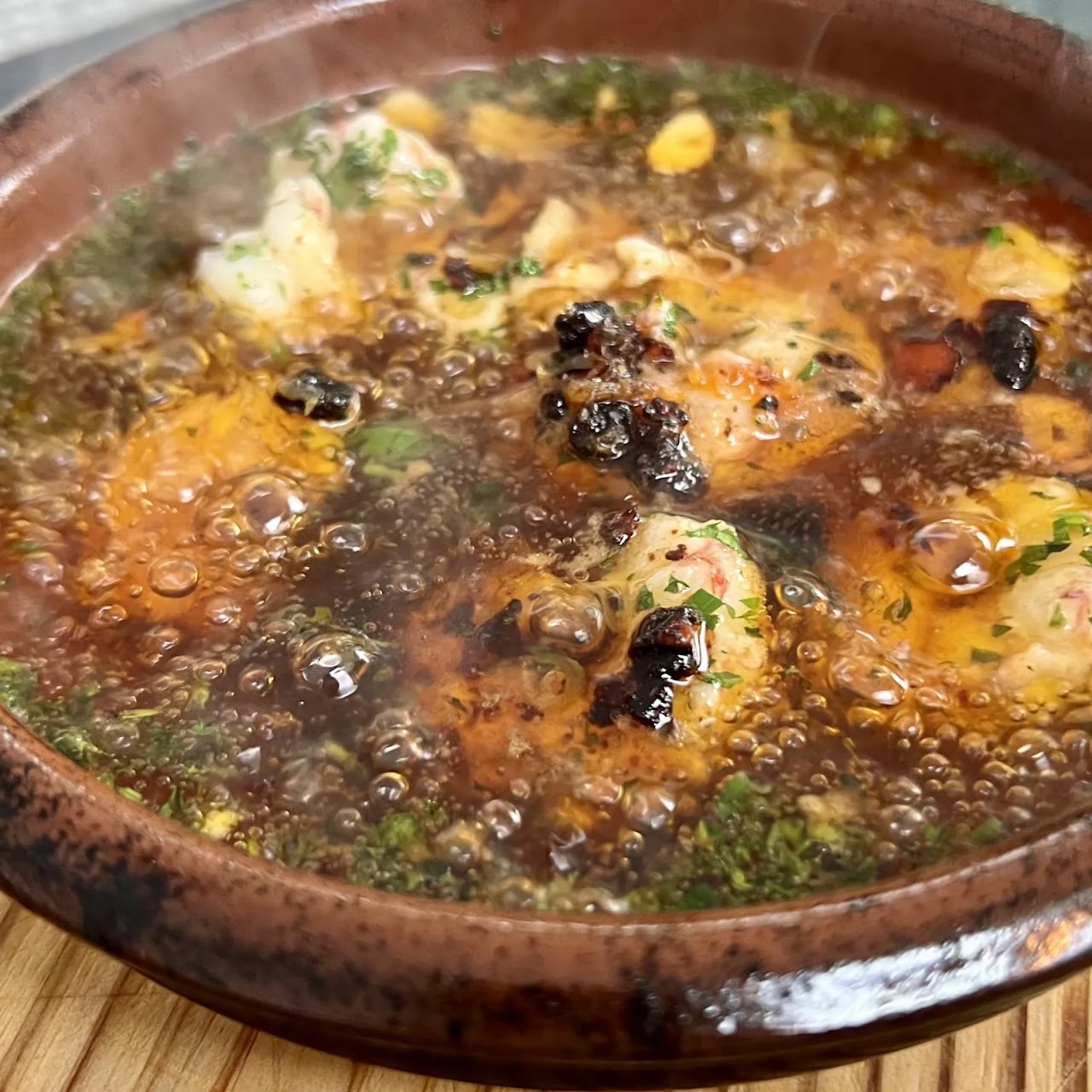 A clay bowl of seafood stew with mussels and shrimp in broth