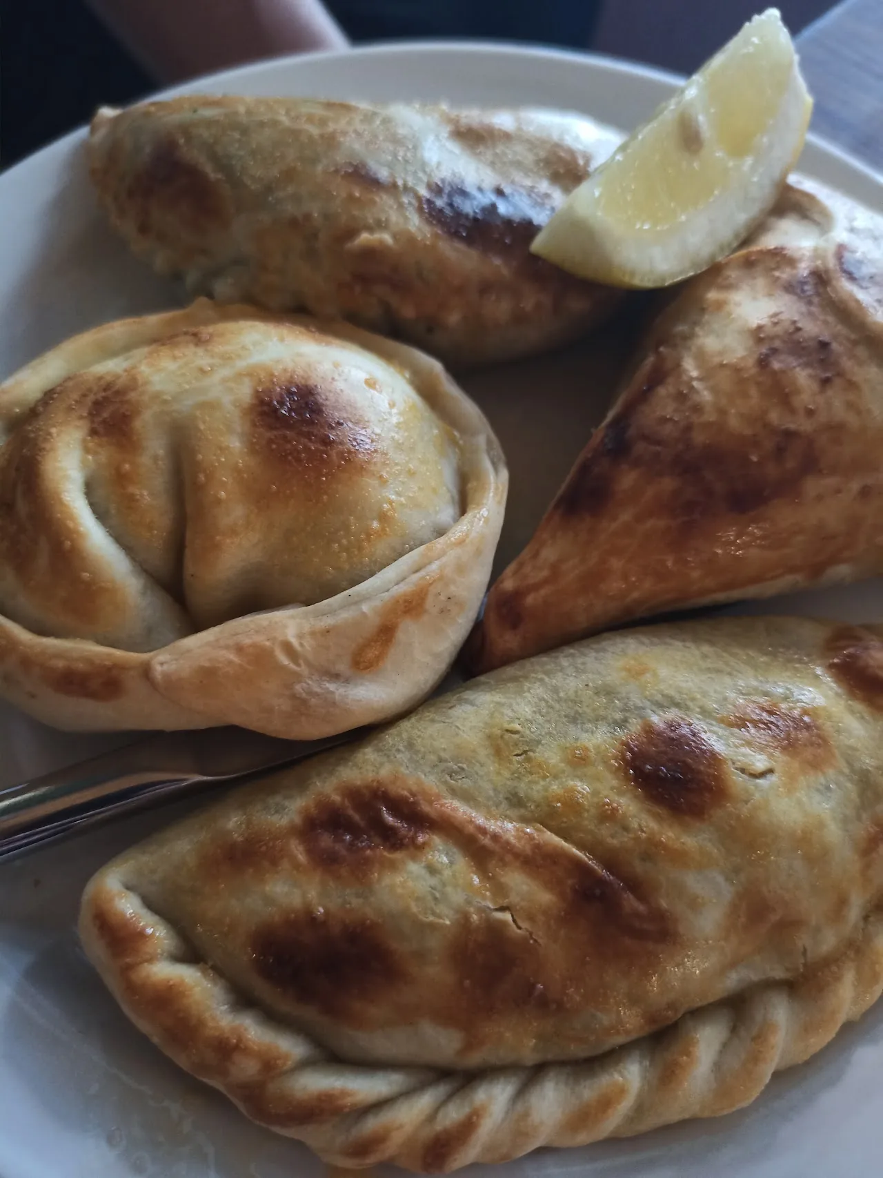 Three golden baked empanadas on a plate with a lemon wedge
