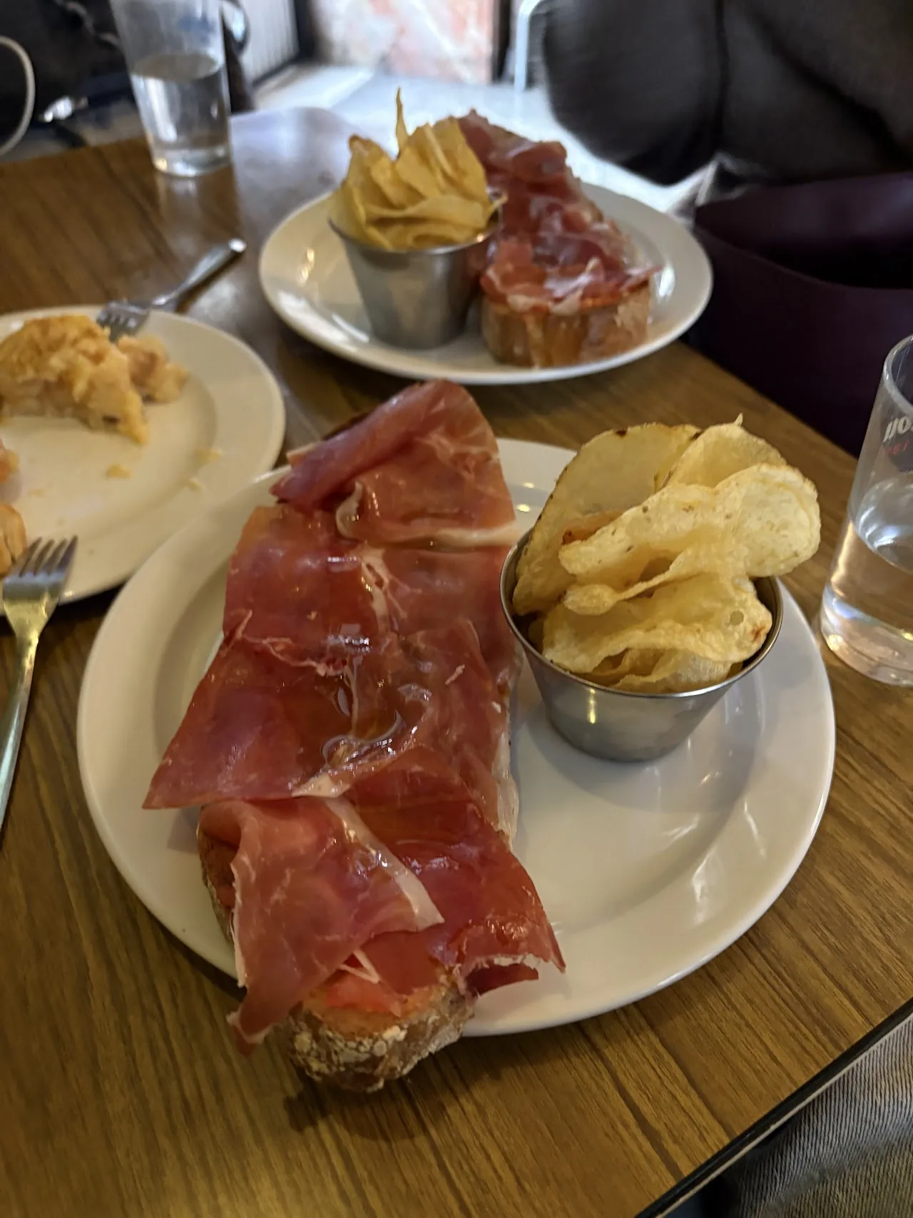 A plate of cured ham slices with a cup of potato chips