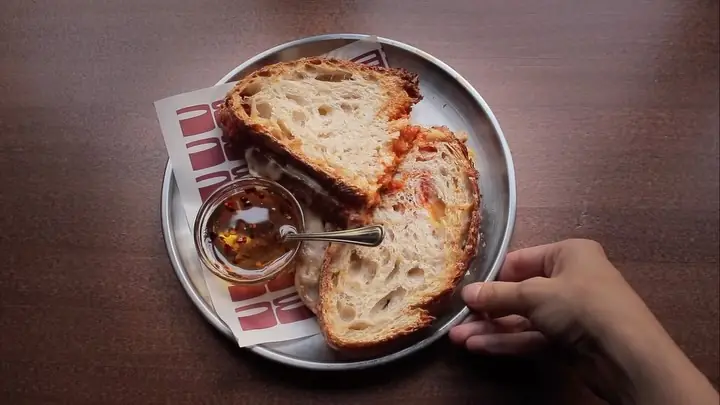 A grilled cheese sandwich cut in half on a metal plate next to a small dish of hot honey with a spoon