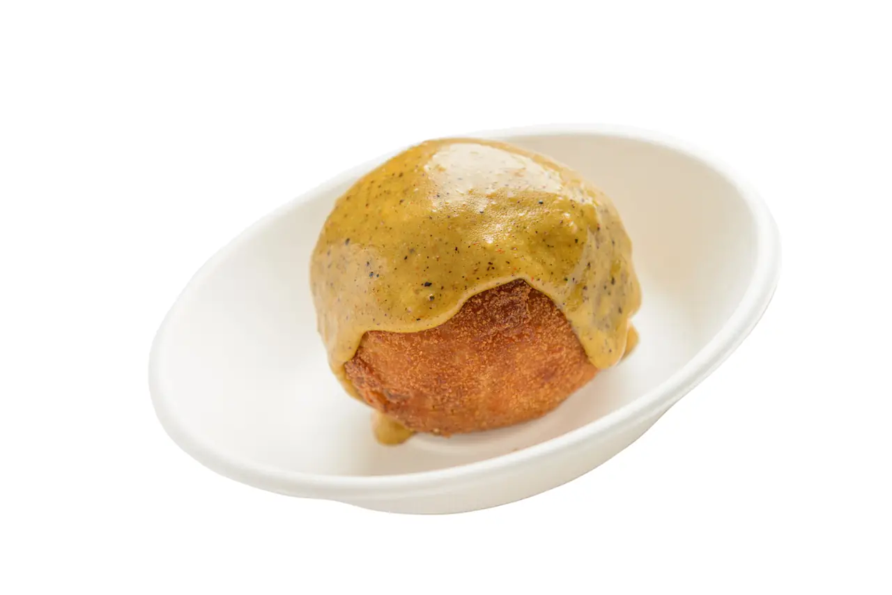 A breaded, deep-fried croquette-style ball topped with a rich mustard-colored sauce, served in a small oval dish, at Bar Córdoba