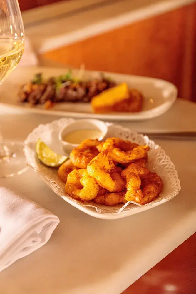 Crispy fried squid rings with a lime wedge and dipping sauce on a lace-paper plate, Bar Costa
