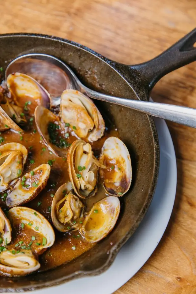 Grilled clams in a spicy tomato-paprika broth with chives, served in a cast-iron skillet at Bar Galán