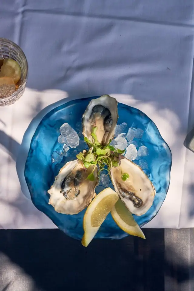 Three freshly shucked oysters on ice with lemon wedges on a blue glass plate at Bar Galán