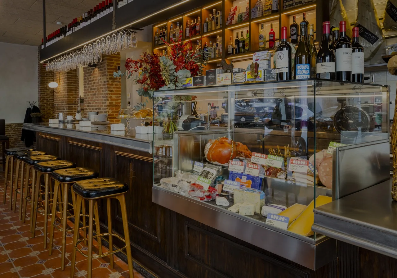 A bar counter with leather stools, a glass deli case and a plate of pastries at the far end