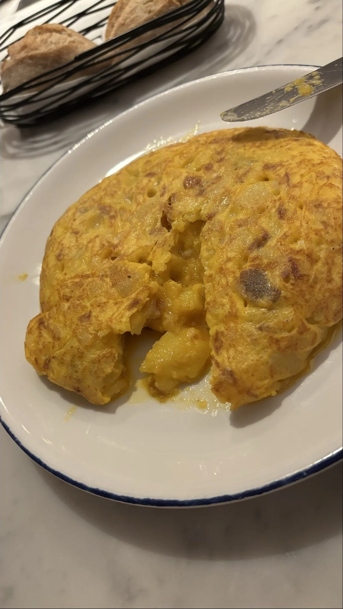 A thick Spanish potato omelette with a slice cut open on a white plate with a blue rim