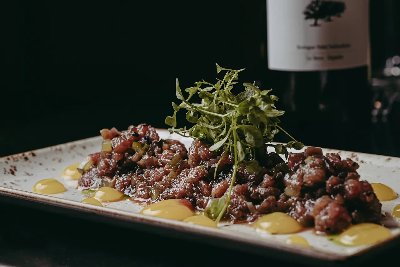 Chopped beef tartare topped with fresh watercress and dotted with mustard sauce on a speckled plate, Bar Michigan