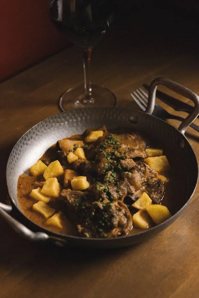 Braised beef stew with diced potatoes and chopped parsley in a metal pan, Bar Nuri