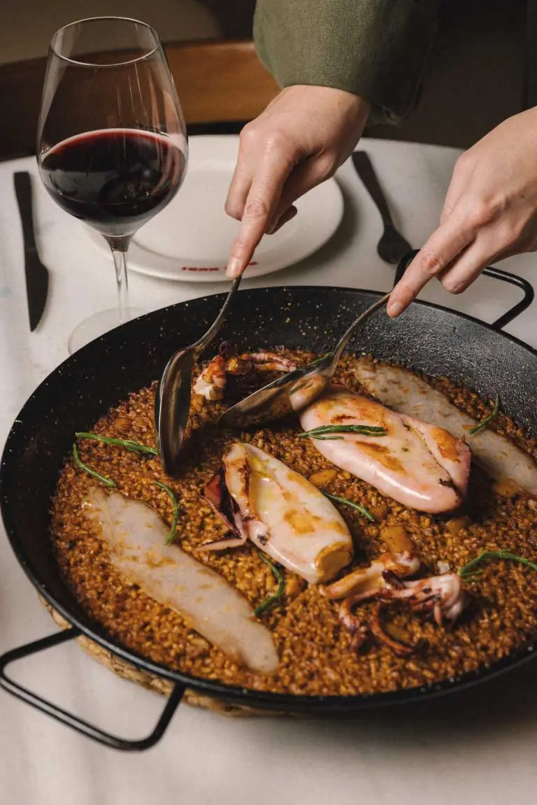 Seafood and rice paella with grilled squid being served from a black pan, Bar Nuri