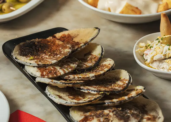 Grilled shellfish on the half-shell, lightly charred, on a black platter.