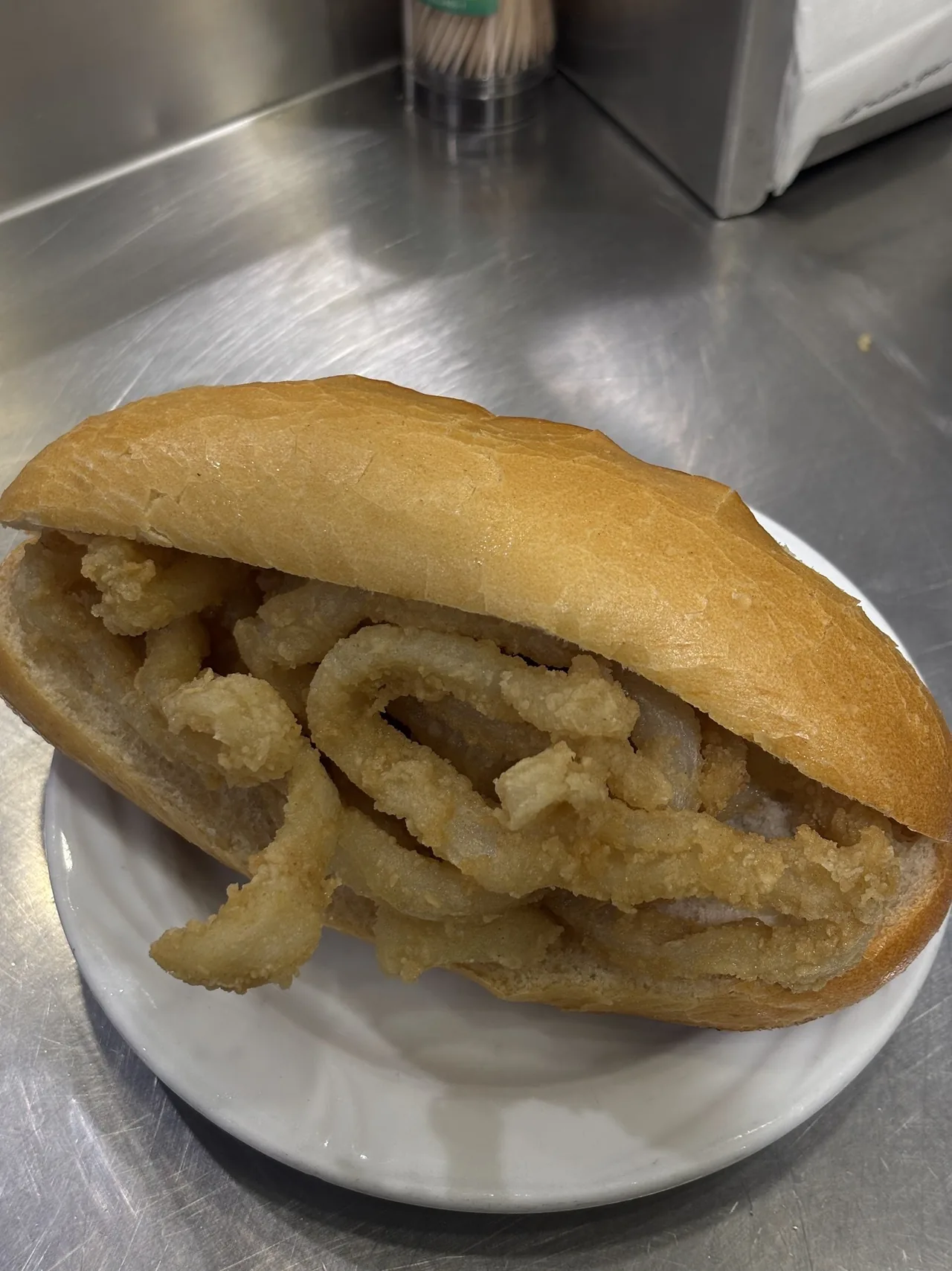 A crusty roll filled with fried squid rings on a white plate