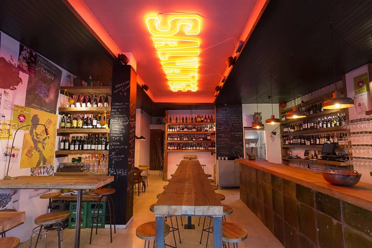 Interior with a glowing SALVATGE neon sign and a wall of wine bottles at Bar Salvatge.