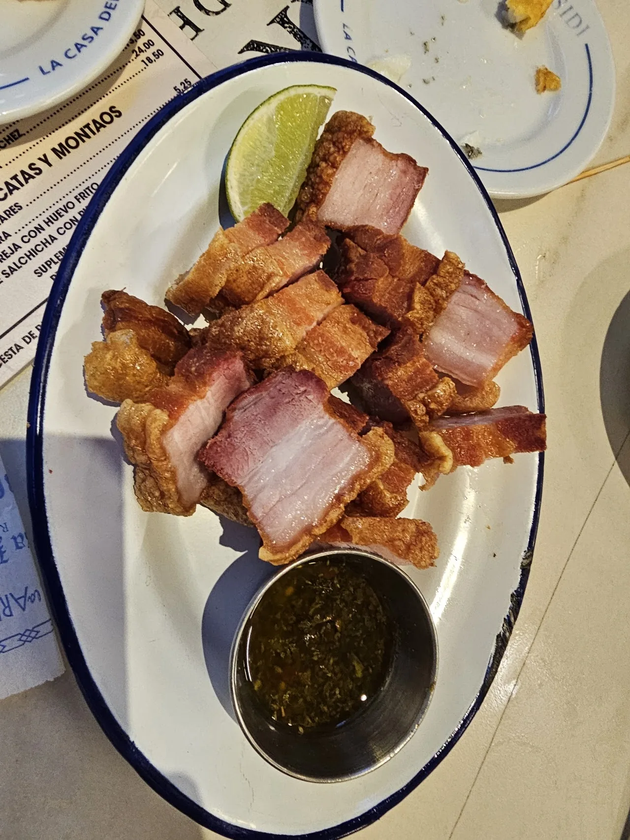 A plate of fried pork belly bites with a dipping sauce and lime