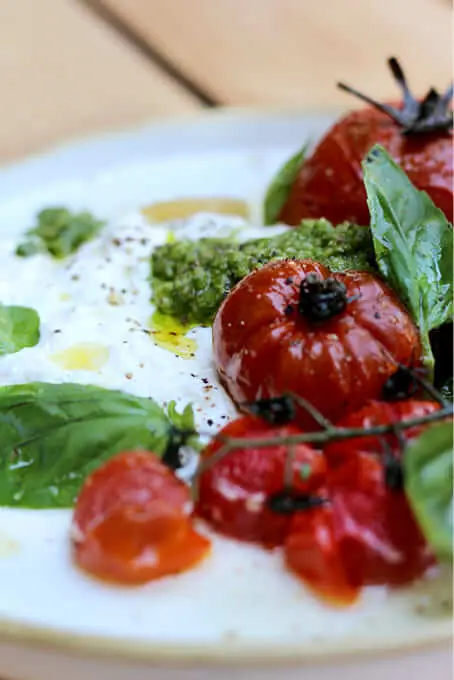 Burrata topped with roasted cherry tomatoes on the vine, pesto, and fresh basil leaves on a white plate, Bar Tomate Barcelona