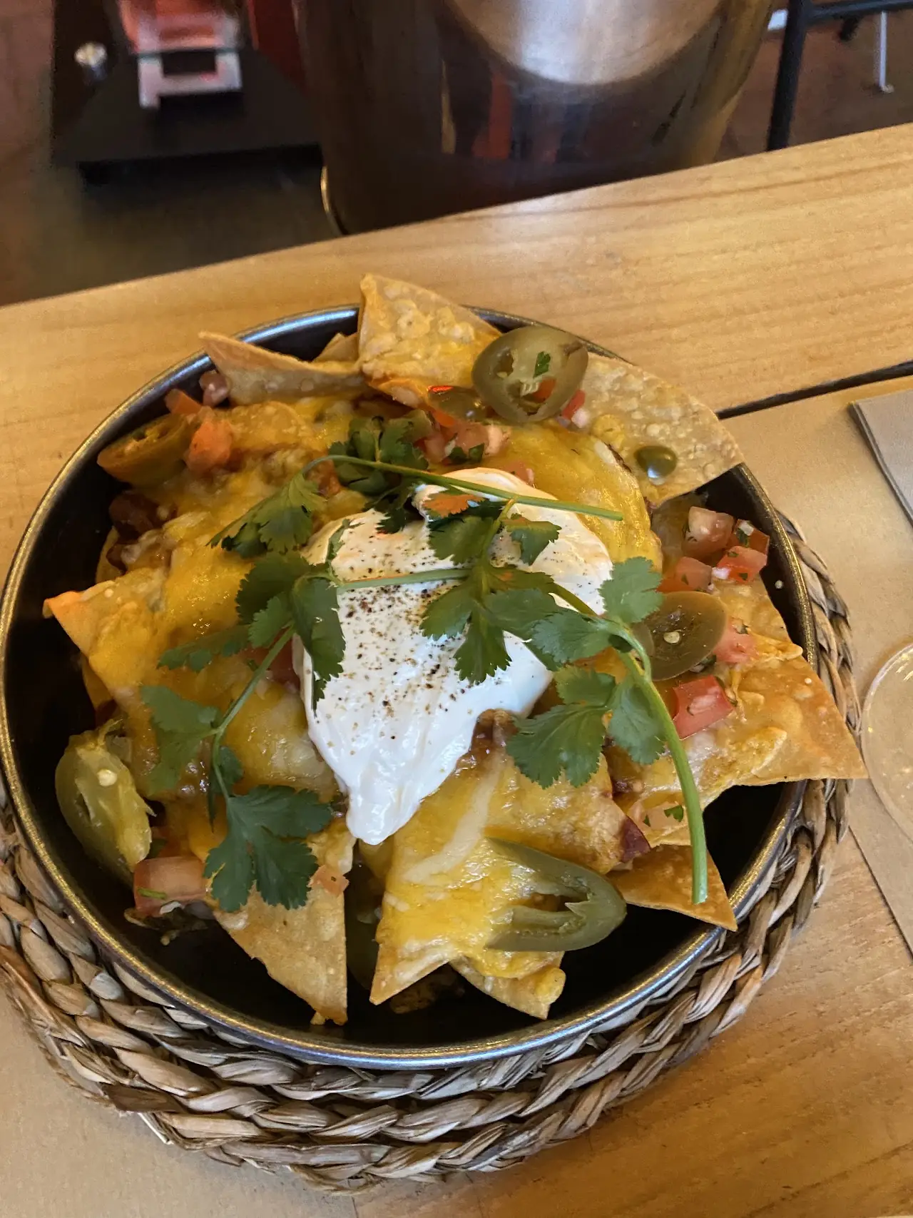 A basket of loaded nachos topped with melted cheese, sour cream and cilantro.