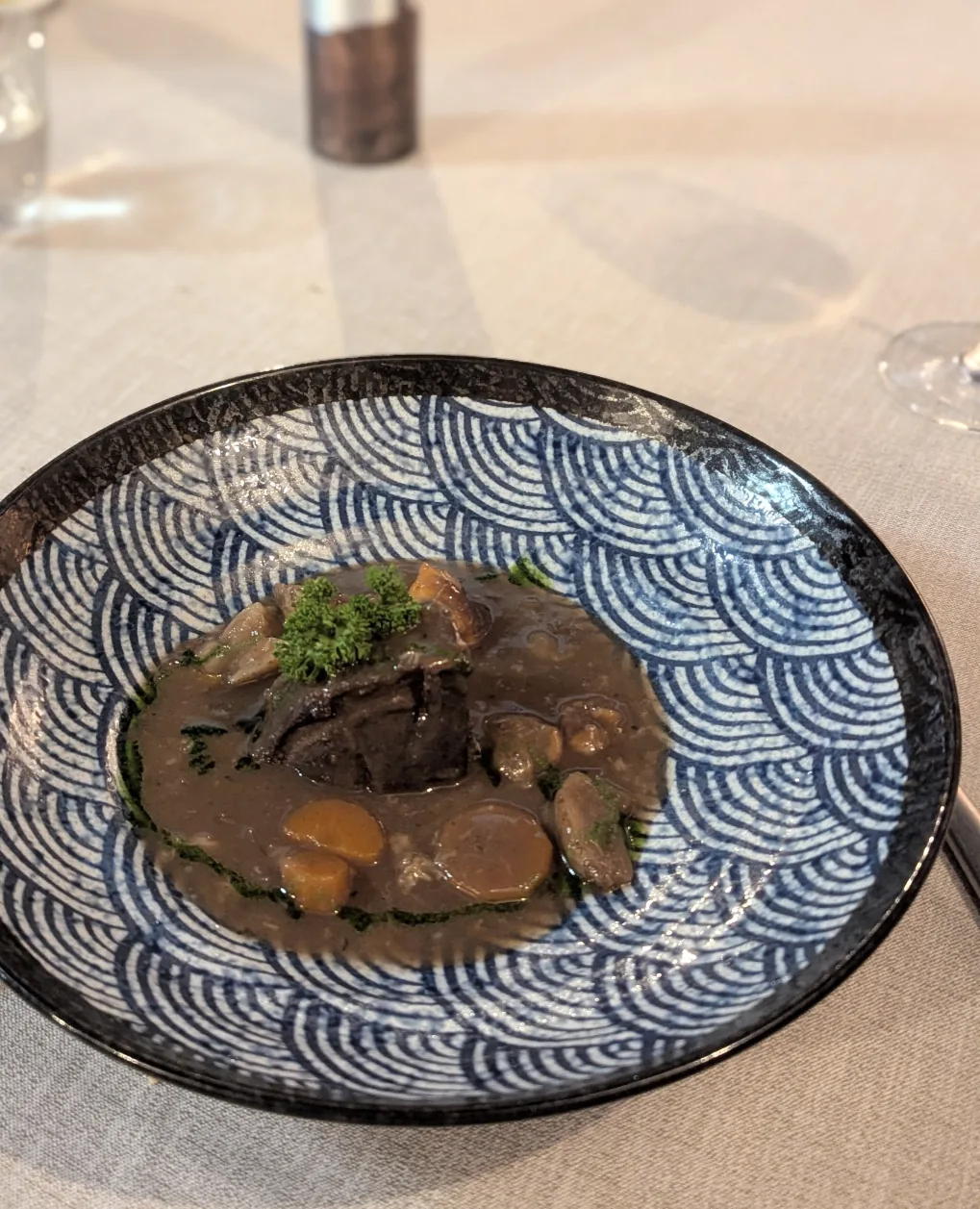 A meat dish with mushrooms in dark sauce on a blue wave-patterned plate