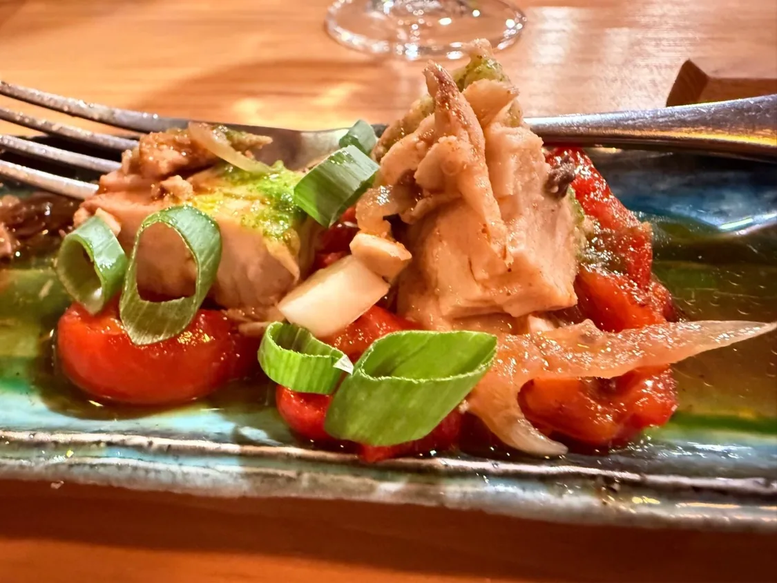 A salad of cherry tomatoes, basil leaves, and crispy strips on a teal plate