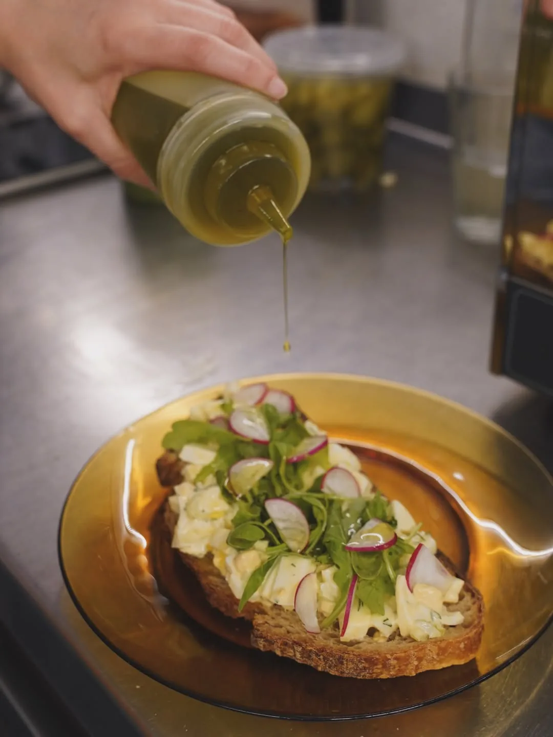 Open-faced toast topped with radish slices and greens, being drizzled with olive oil