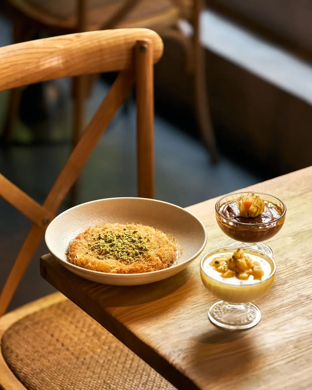 Kanafeh pastry with crushed pistachio beside two dessert cups with fruit and cream toppings