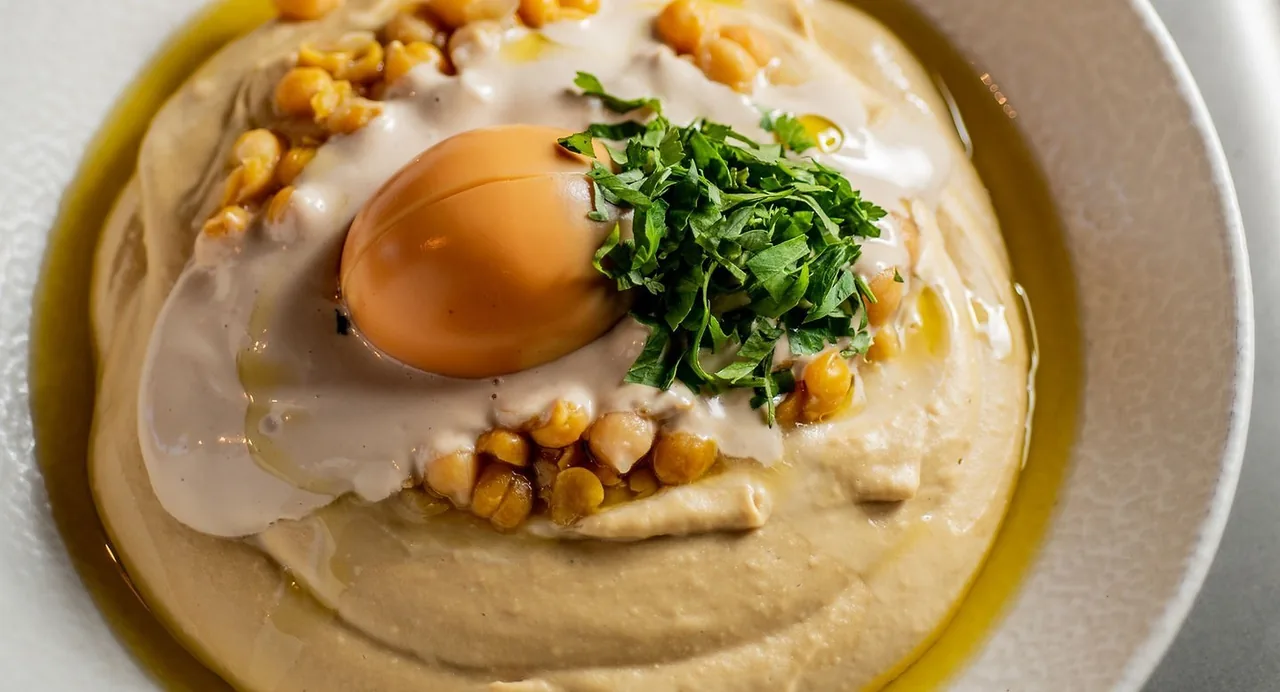 A plate of smooth hummus topped with an egg yolk, chickpeas, herbs and olive oil