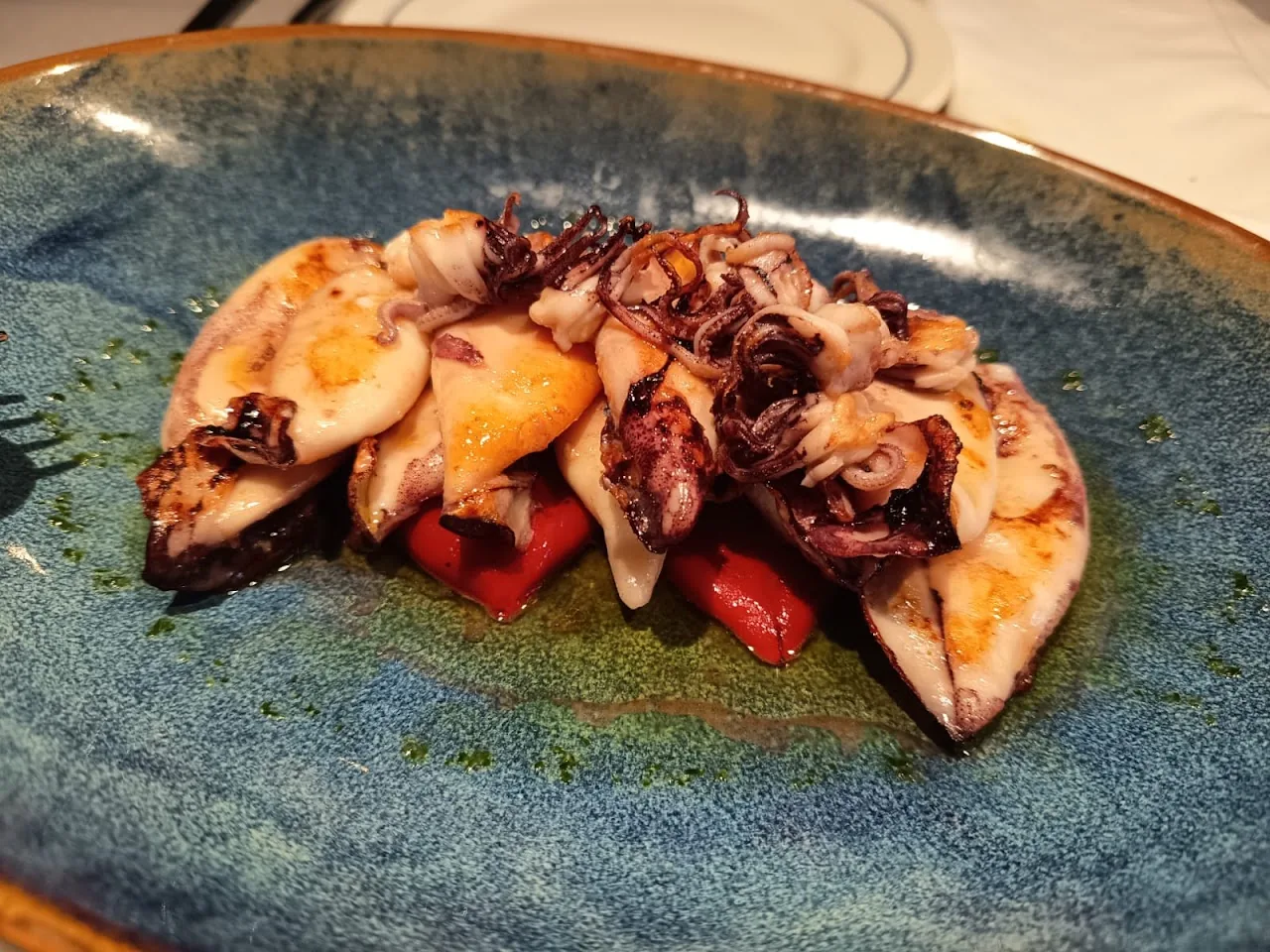 Grilled octopus and squid with charred red pepper on a blue plate