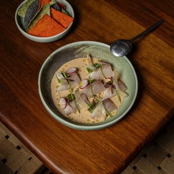 A green bowl of sliced raw fish in a pale sauce on a wooden board
