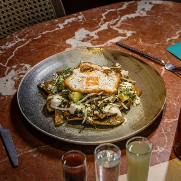 A round plate of crispy tortilla pieces topped with vegetables and a fried egg
