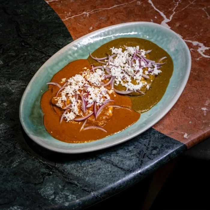 An oval teal plate of two sauces, one orange and one green, topped with crumbled white cheese and red onion