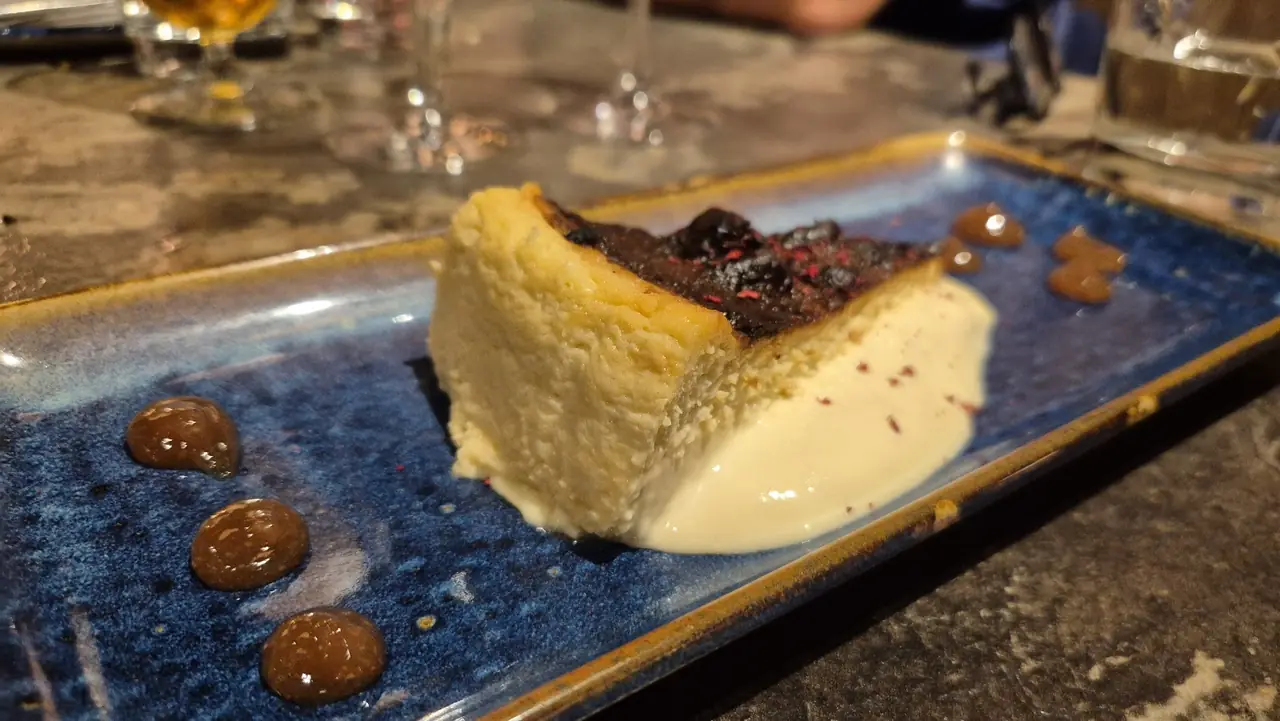 Slice of burnt Basque cheesecake with berry compote and cream on a blue plate