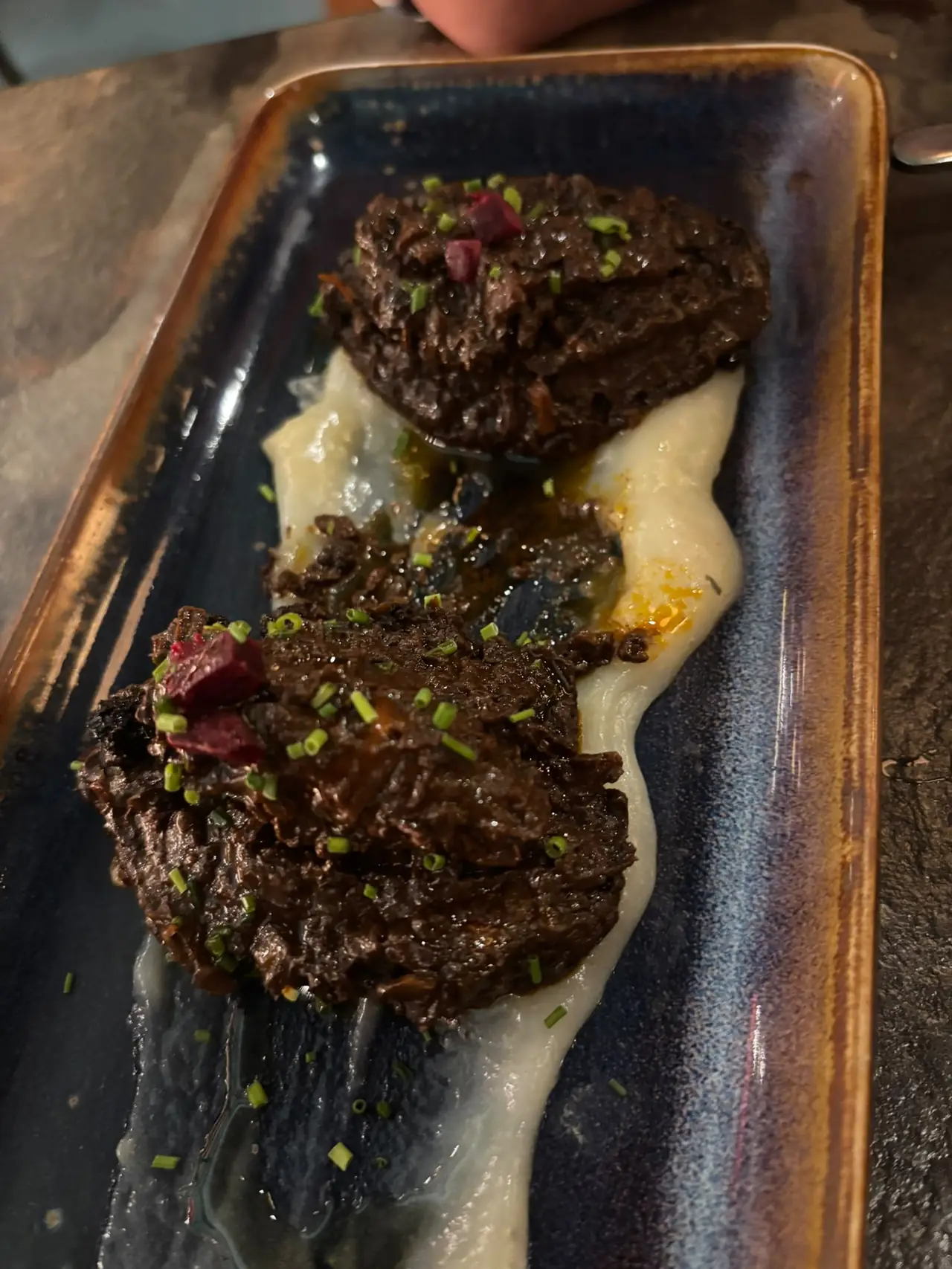 Two seared morcilla cakes with chive and beet garnish over a creamy sauce