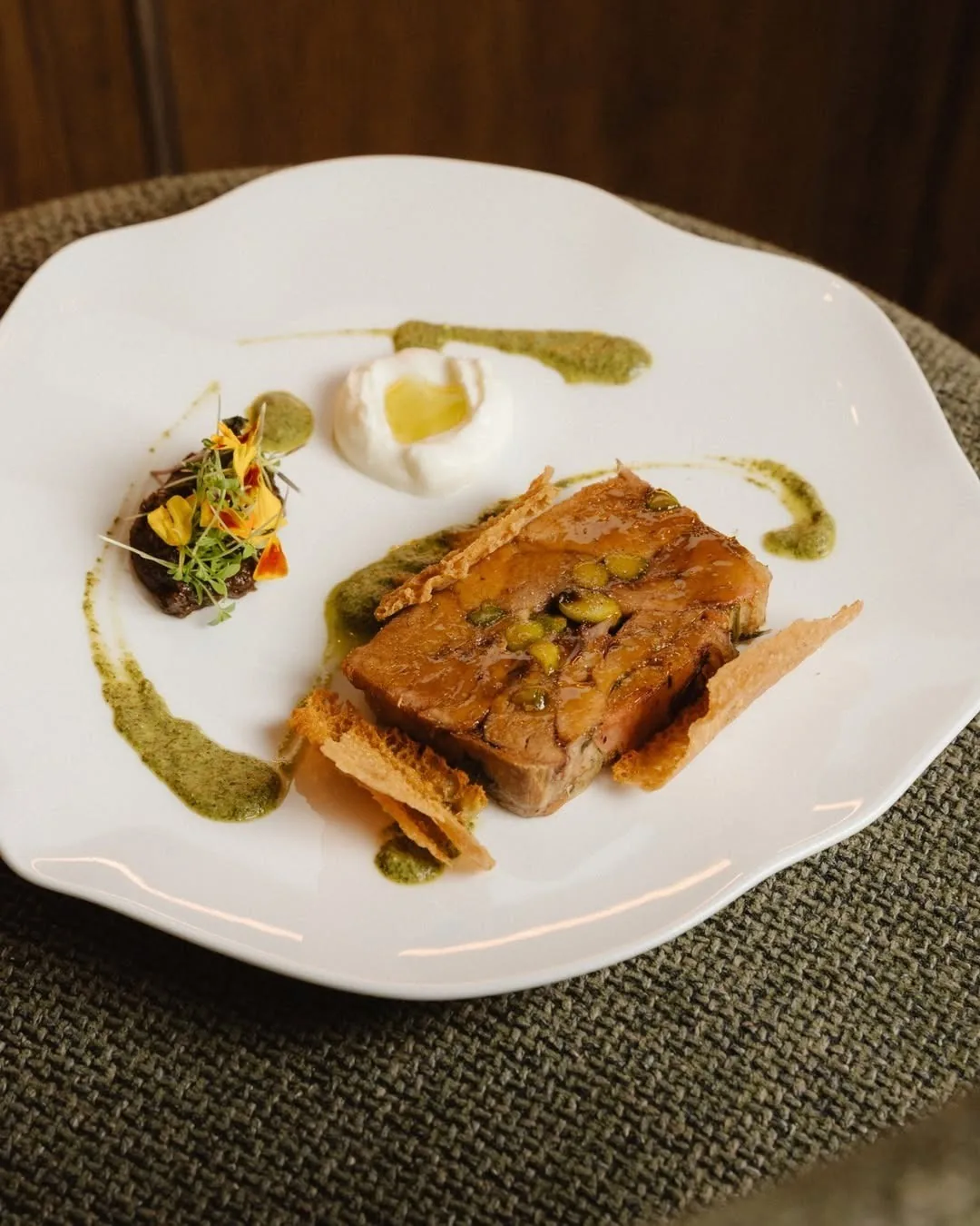 A layered savoury pastry with a green sauce and a small salad on a white plate