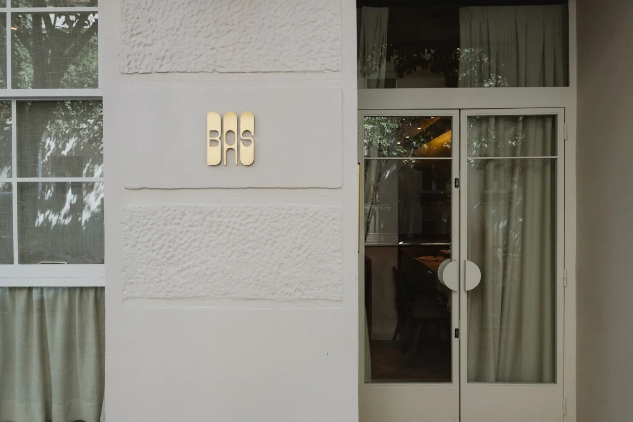 A pale stone facade with a small gold sign between two glazed doors