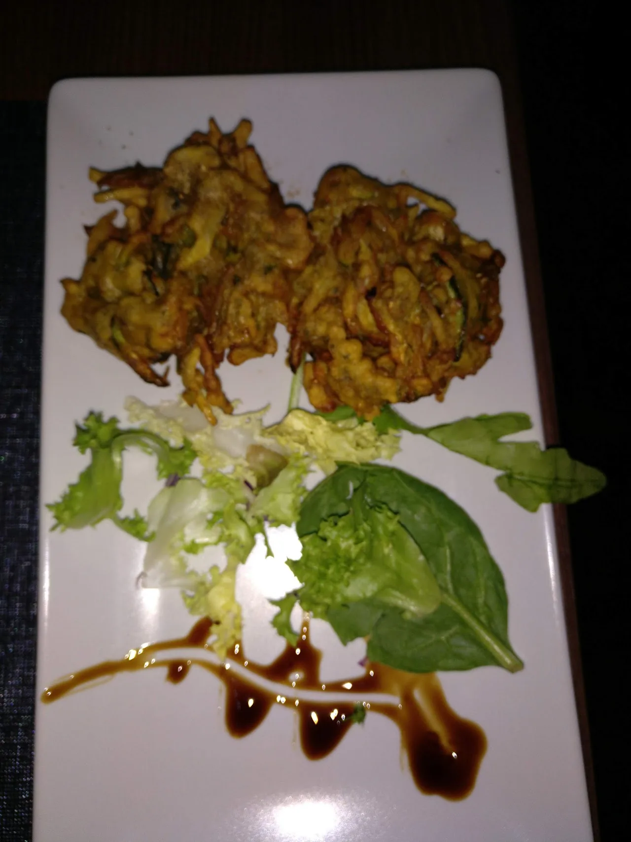 Fried vegetable pakora fritters on a plate with lettuce and a tamarind drizzle