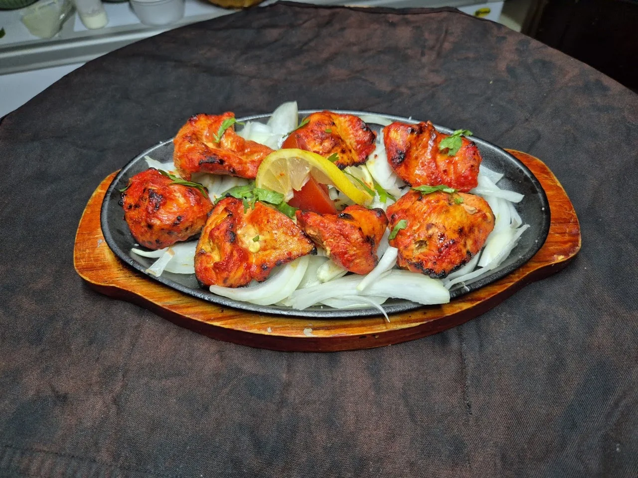 Skewered tandoori chicken tikka pieces on a platter with onions and lime