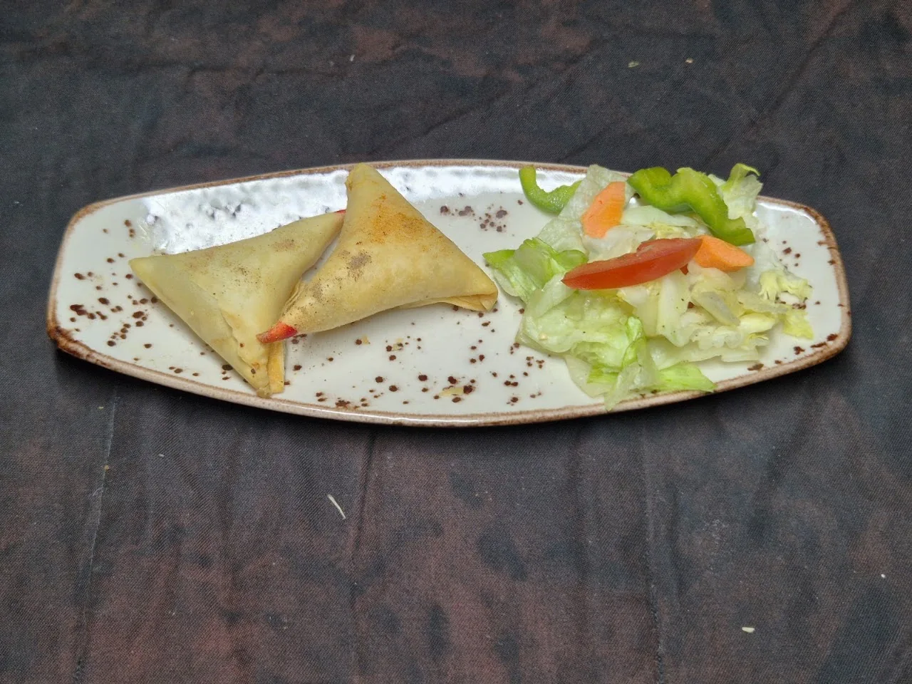 Two golden samosas on a plate with a side salad